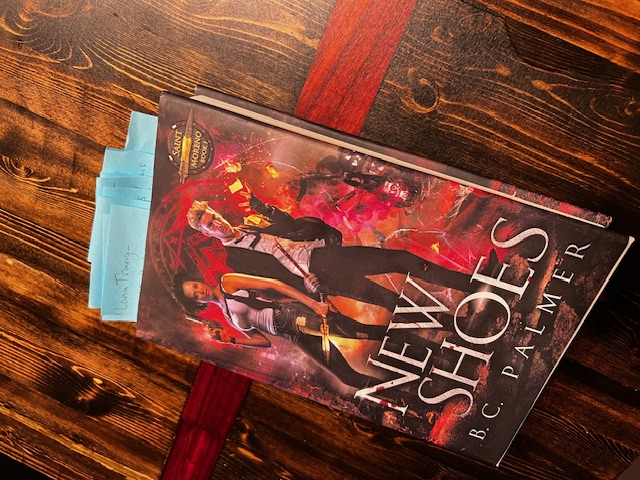 A paperback copy of New Shoes by B.C. Palmer on a wooden table, bristling with sticky notes.